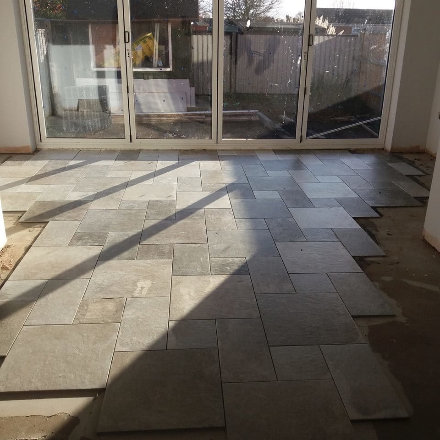 Stone floor tiles being laid across a bright extension