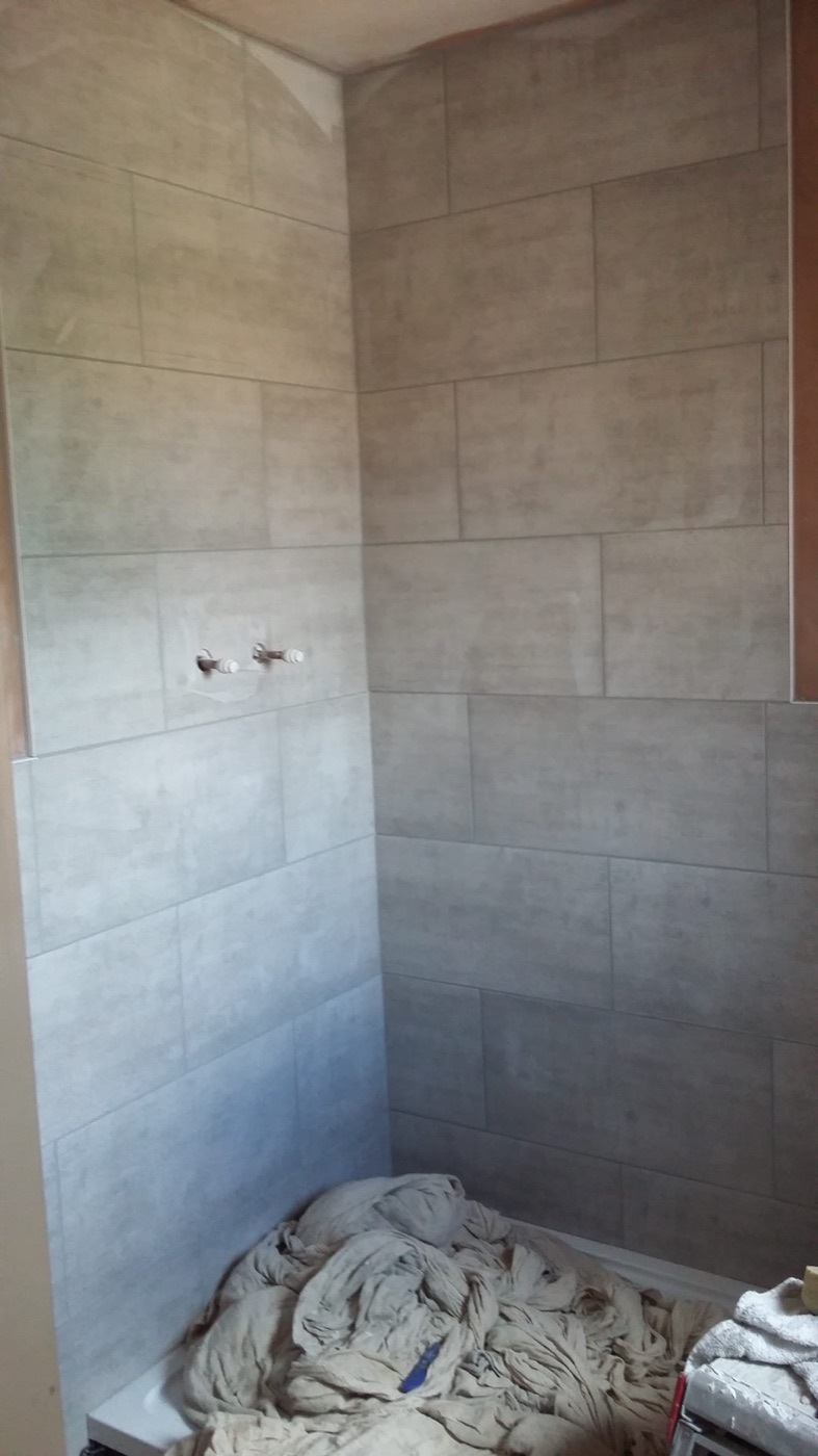Bathroom wall tiled in large grey format, ready for fittings